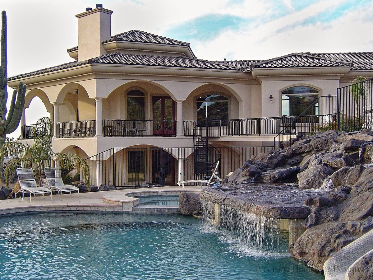 Luxury Mediterranean custom home with pool, spa, waterfall, and desert landscaping under a bright sky.