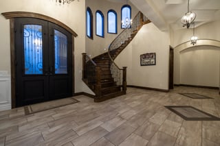 Elegant custom home foyer with black double doors, curved wood staircase, and arched windows.