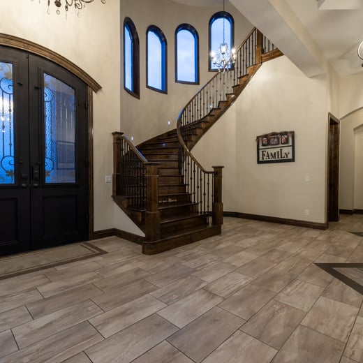 Elegant custom home foyer with black double doors, curved wood staircase, and arched windows.
