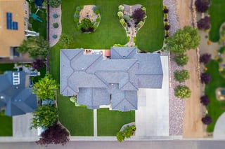 Aerial view of a custom home with gray roof, landscaped yard, green lawn, and wide driveway.