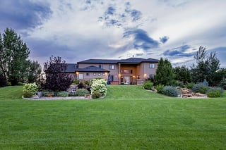 Custom home with illuminated windows overlooking a manicured green lawn at dusk.