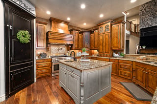 Warm custom home kitchen with granite island, wood cabinets, and stainless steel appliances.