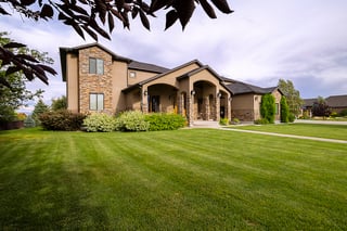 Elegant custom home with stone accents, lush green lawn, and covered front porch under a bright sky.