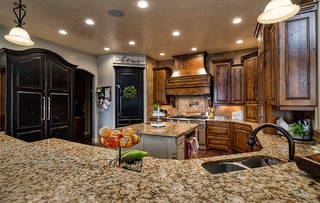 Custom home kitchen with granite island, wood cabinets, stainless sink, and warm ambient lighting.