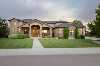 Elegant custom home with stone accents, lit porch, and manicured lawn at dusk.
