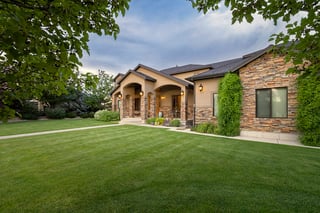 Custom home with stone columns, arched porch, and manicured lawn under soft evening light.