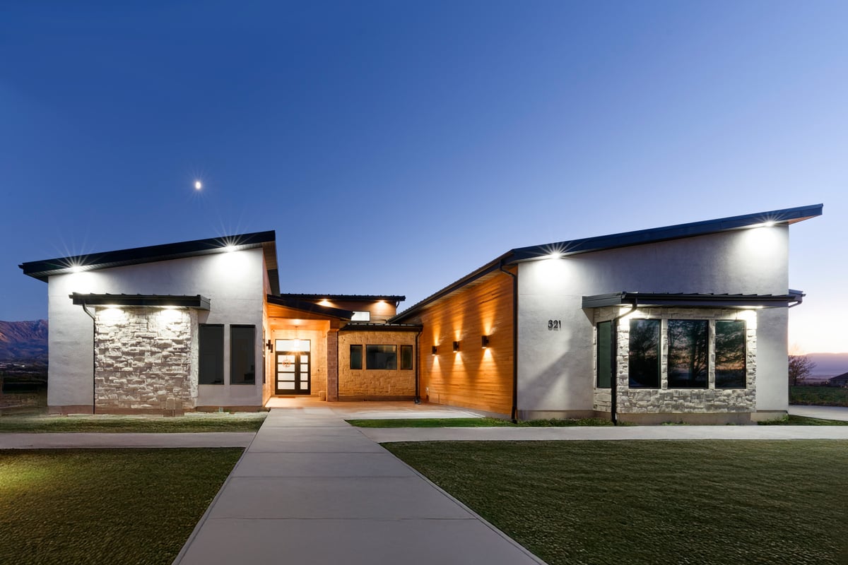 Modern custom home at dusk with stone accents, warm lighting, and a clear blue evening sky.