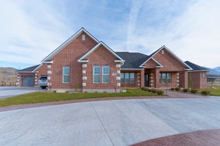 Red brick custom home with gabled roof, stone accents, large driveway, and mountain views.