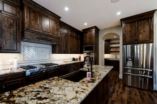 Luxury custom home kitchen with dark wood cabinets, granite island, and stainless steel appliances.