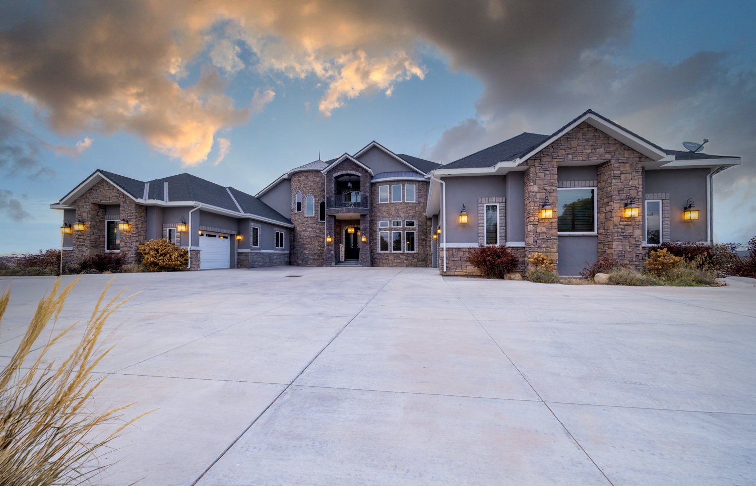 Elegant custom home with stone tower, three car garage, and wide driveway at sunset.