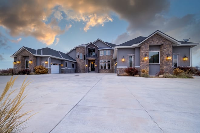 Elegant custom home with stone tower, three car garage, and wide driveway at sunset.