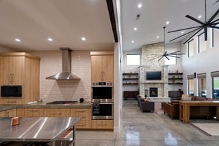 Modern open concept custom home kitchen and living room with stone fireplace and polished concrete floors.