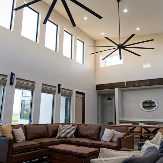 Spacious custom home living room with leather sectional, tall windows, ceiling fans, and modern farmhouse décor.