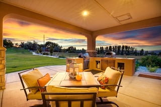 Outdoor patio with lounge seating and kitchen featuring pizza oven at sunset in a custom home.