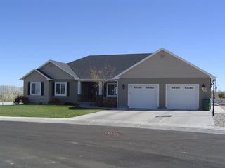 Modern custom home with gray exterior, two-car garage, driveway, and basketball hoop on suburban street.