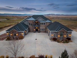 Luxury custom home with stone facade, illuminated driveway, and scenic countryside views at twilight.