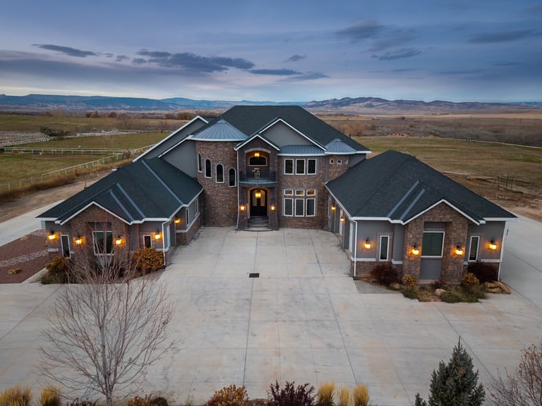 Luxury custom home with stone facade, illuminated driveway, and scenic countryside views at twilight.