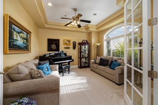 Elegant custom home living room with beige sofas, grand piano, blue accents, and sunlight through French doors.