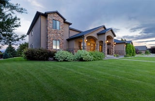 Elegant custom home at dusk with stone and stucco exterior, glowing porch lights, and manicured lawn.