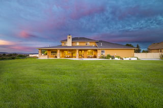 Custom home with covered patio and glowing windows at twilight under a dramatic colorful sky.